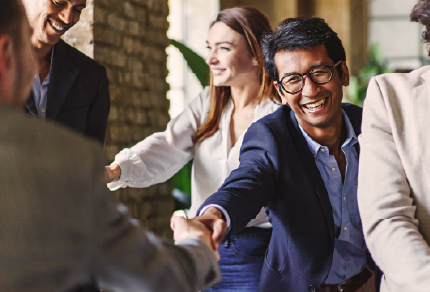 Two people shaking hands while smiling, with more people around them.